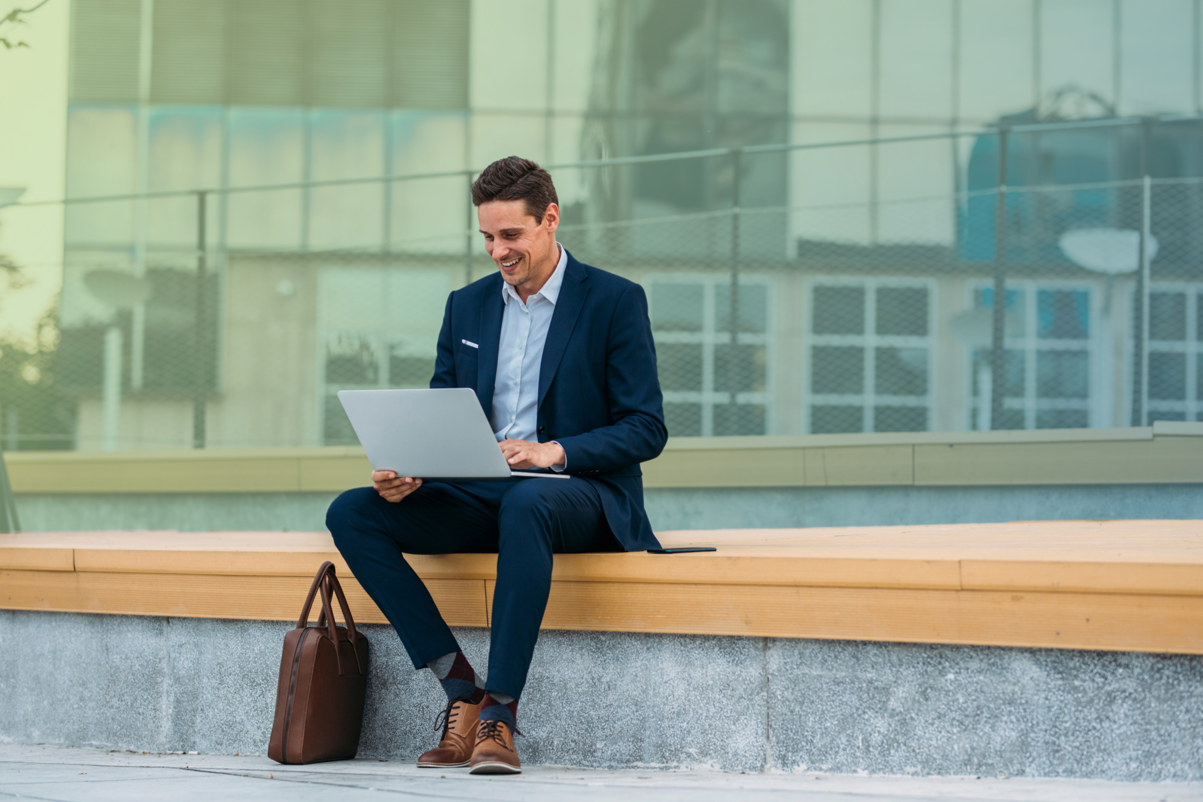 business man sitting on an outside bench looking at his laptop